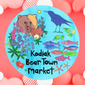 A colorful illustration of a bear, a raven, flowers, and fish with the text Kodiak Bear Town market on a blue circle, set against a red background decorated with white and striped heart shapes.